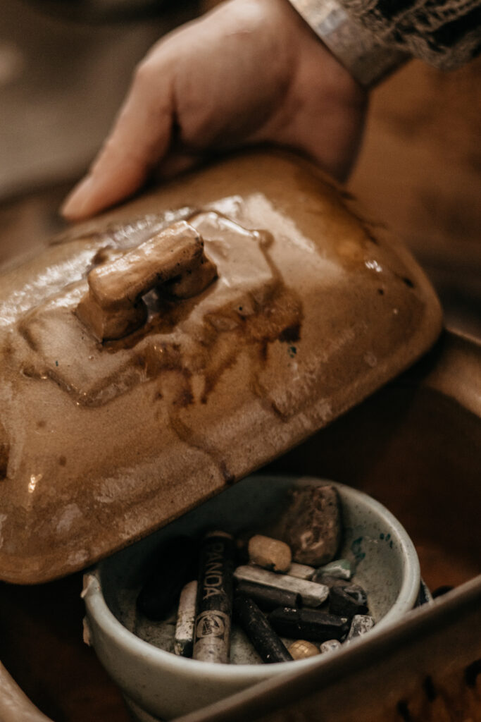 Hand of artist Leonoor Ruigrok beside a container of charcoal in her studio