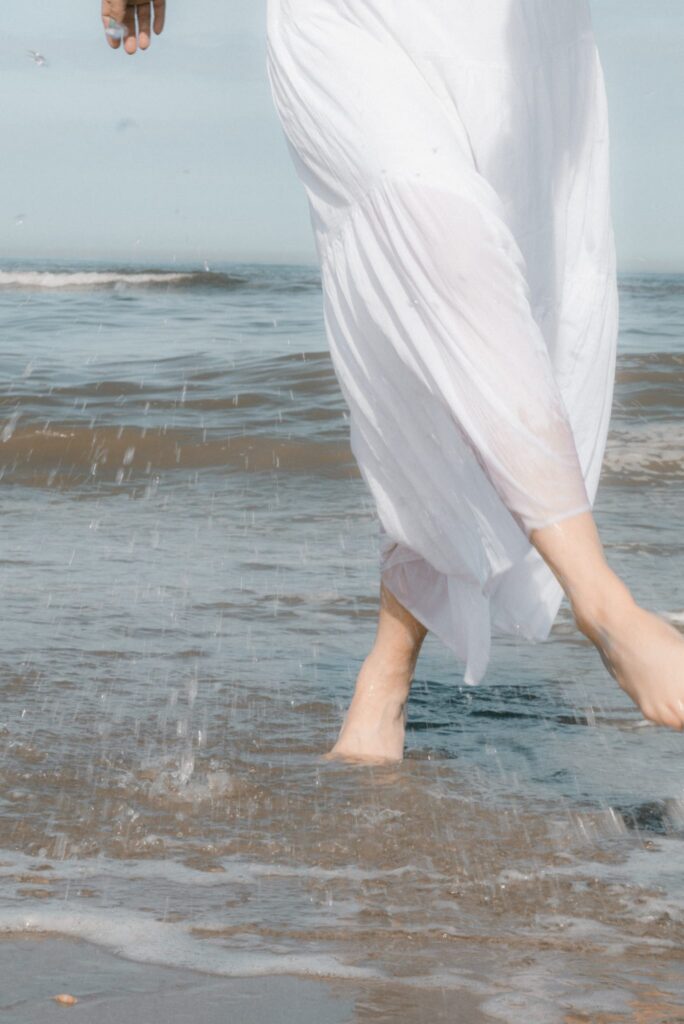 Bare feet moving through shallow seawater beneath flowing white fabric, splashing water and expressing release, movement and letting go. Female artist Leonoor Ruigrok - Noordwijk