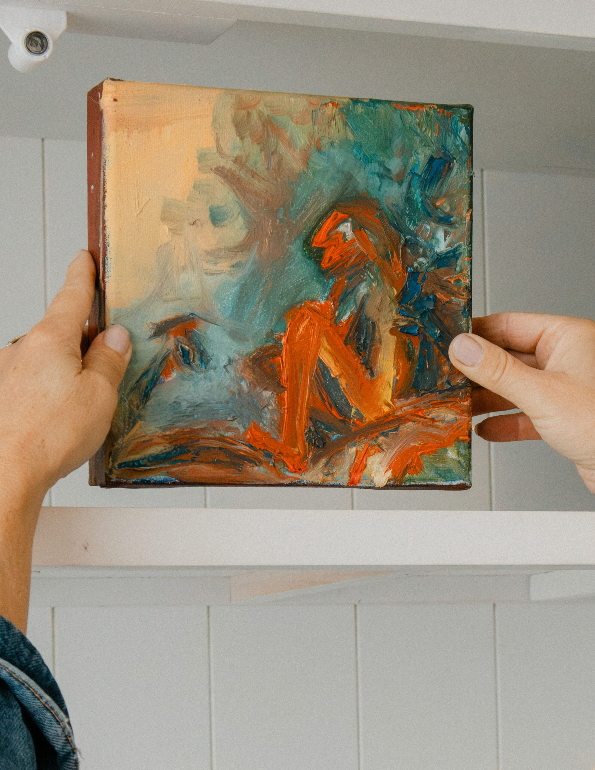 Leonoor Ruigrok holding a small colourful painting in front of a shelf in her studio.