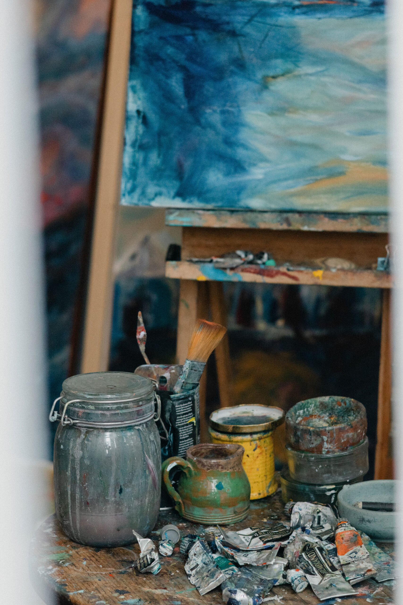 Paint jars, brushes and used paint tubes beneath a blue painting in Leonoor Ruigrok’s studio